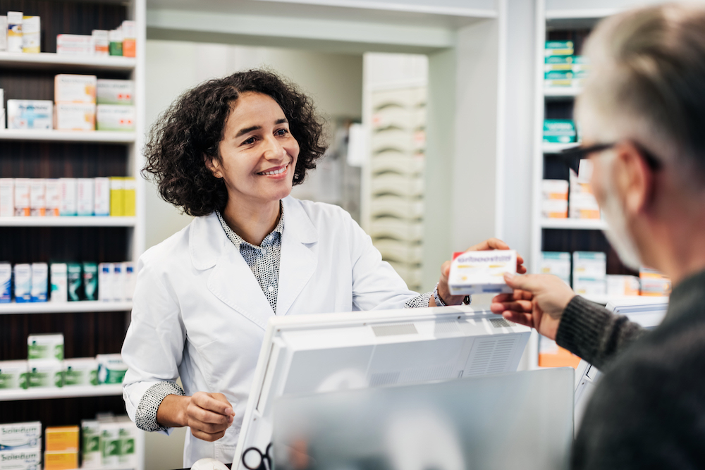 A pharmacist behind the counter, smiling while handing a customer his prescription medicine.